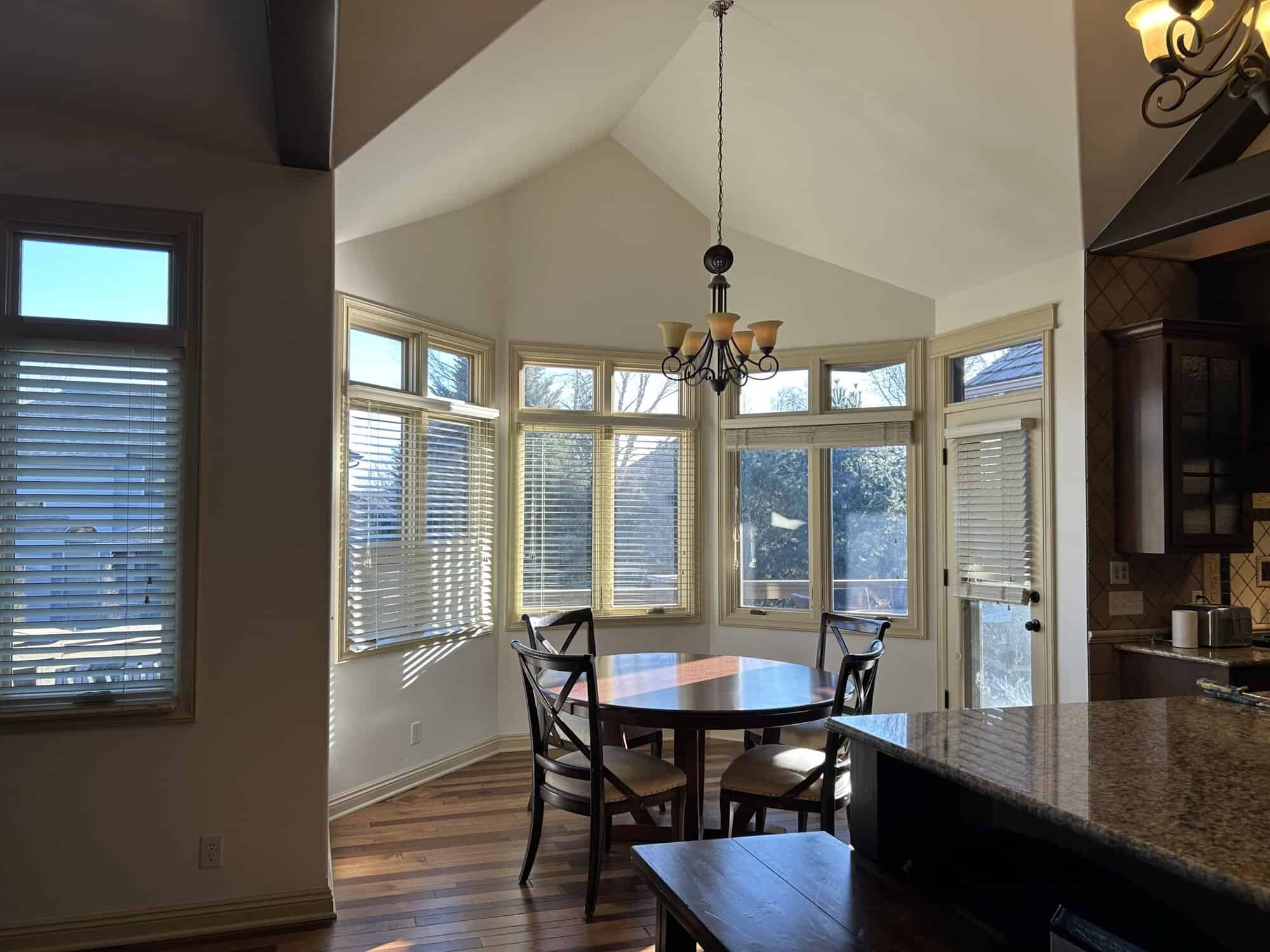 A beautifully painted bright dining room with vaulted ceilings, large windows, and a round wooden table.