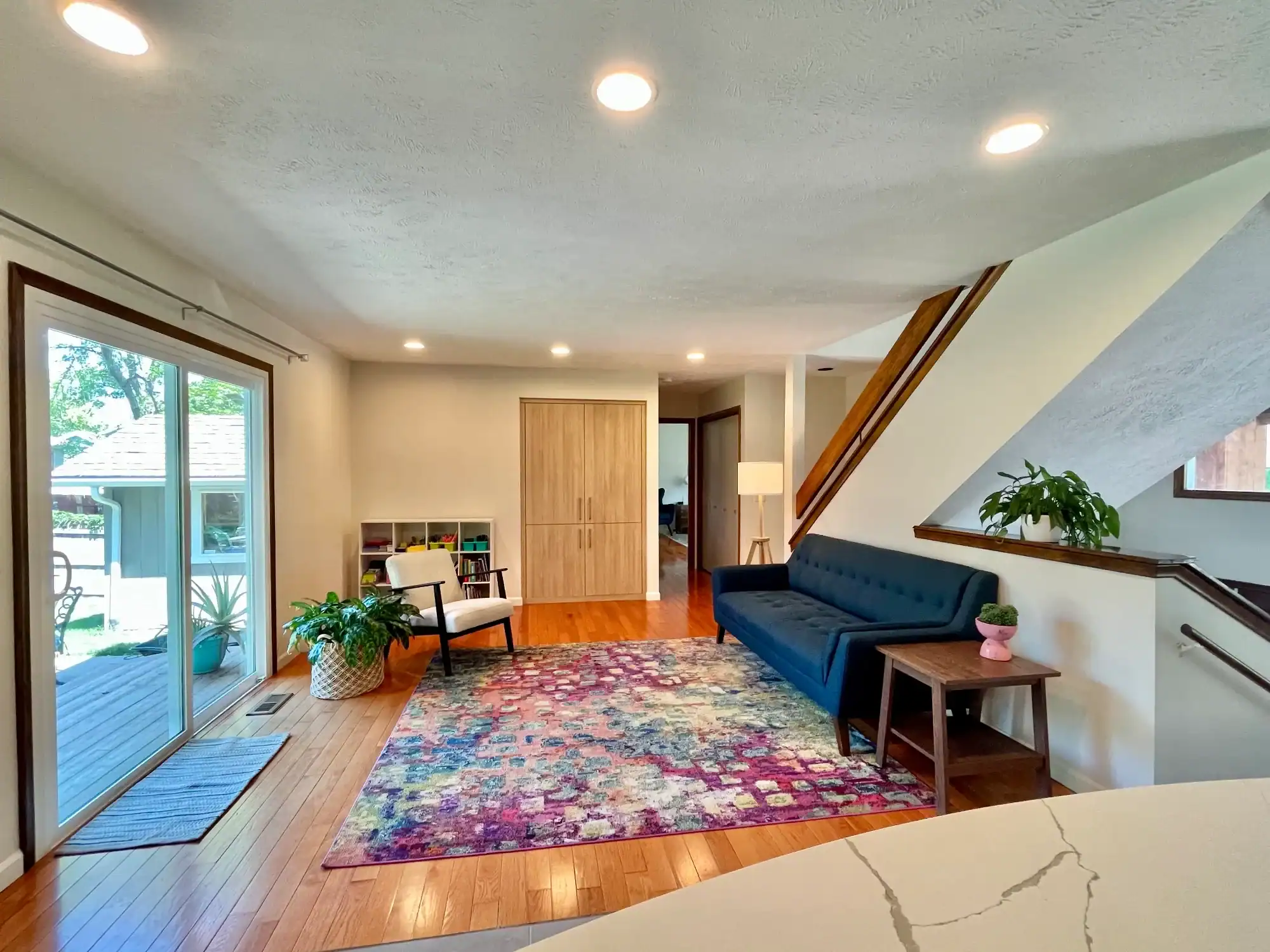 Cream Sitting Room With Staircase Cream painted sitting room with textured ceiling, recessed lighting, wood staircase, navy sofa, and hardwood flooring in
