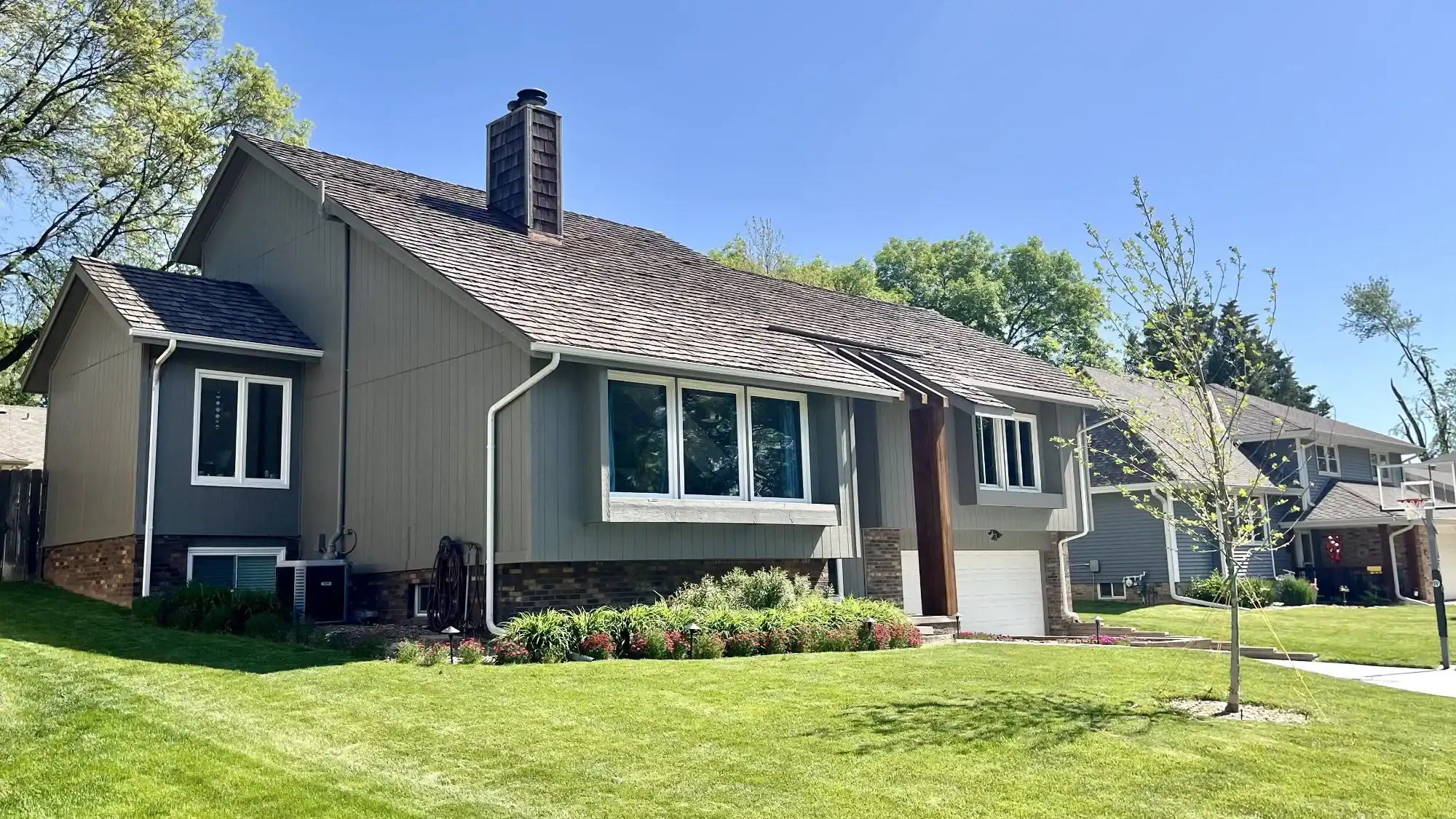 Exterior Front After Residential Painting Gray and tan horizontal siding residential home with white trim, brick foundation, dark roof, and white garage door in Omaha